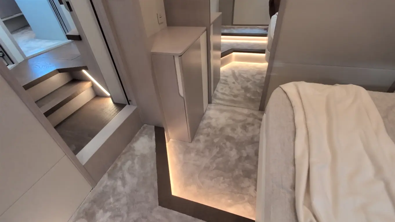 Interior view of a stylish bedroom with soft lighting, elegant furniture, and carpeting, featuring a visible staircase.
